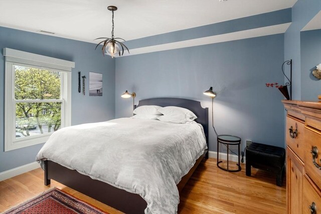 bedroom with baseboards, light wood finished floors, a notable chandelier, and visible vents