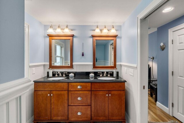 bathroom featuring wood finished floors, double vanity, a sink, and a wainscoted wall
