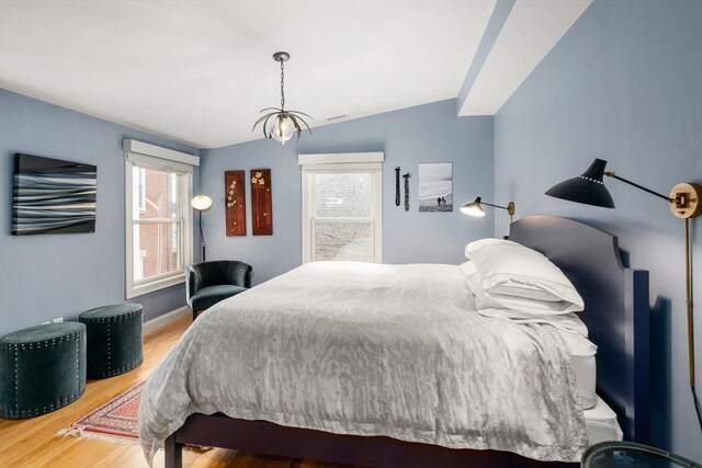 bedroom featuring baseboards, vaulted ceiling, multiple windows, and wood finished floors