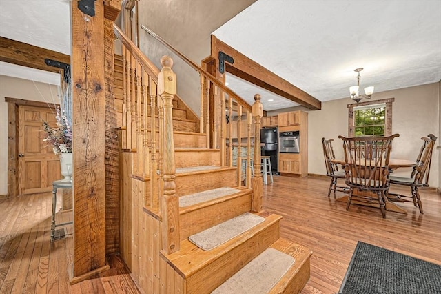 staircase with an inviting chandelier, hardwood / wood-style flooring, and beamed ceiling