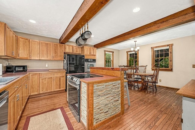 kitchen featuring a chandelier, light wood-type flooring, appliances with stainless steel finishes, pendant lighting, and beam ceiling