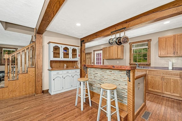 kitchen featuring wood walls, beamed ceiling, sink, a breakfast bar area, and light hardwood / wood-style floors