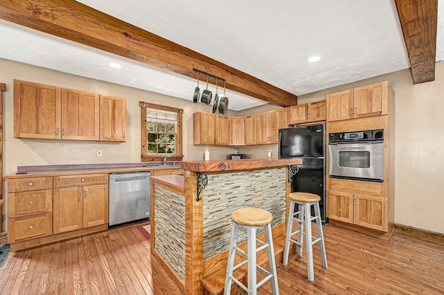 kitchen with appliances with stainless steel finishes, beamed ceiling, sink, a kitchen bar, and light hardwood / wood-style floors