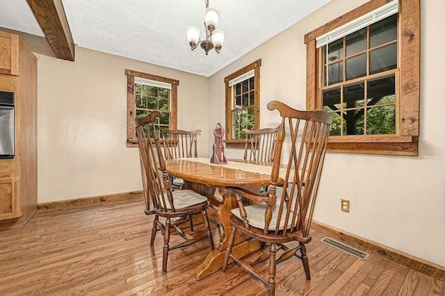 dining room featuring beamed ceiling, an inviting chandelier, and light hardwood / wood-style floors