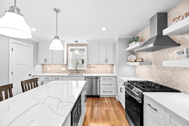 kitchen with a sink, open shelves, appliances with stainless steel finishes, hanging light fixtures, and wall chimney range hood