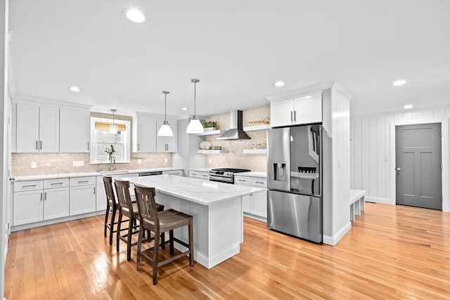 kitchen with white cabinetry, a kitchen bar, a sink, wall chimney range hood, and appliances with stainless steel finishes