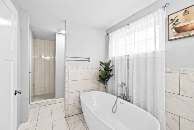bathroom featuring marble finish floor, a freestanding bath, a tile shower, and tile walls