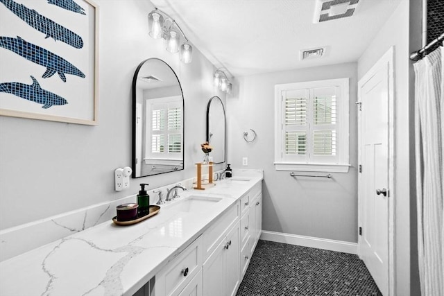 bathroom featuring baseboards, double vanity, visible vents, and plenty of natural light