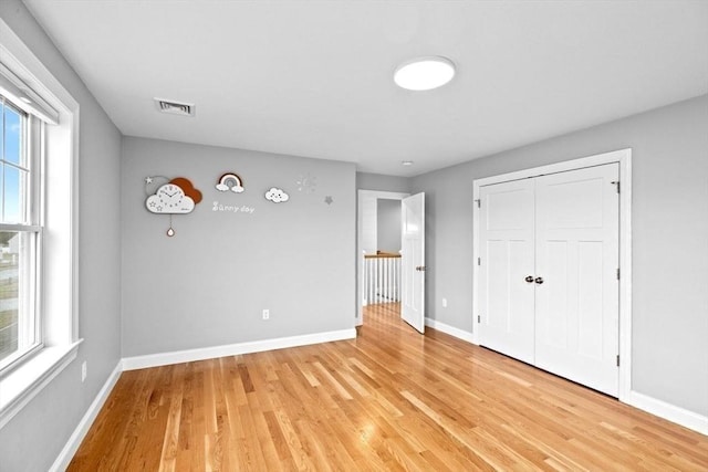 unfurnished bedroom with baseboards, light wood-style flooring, visible vents, and a closet
