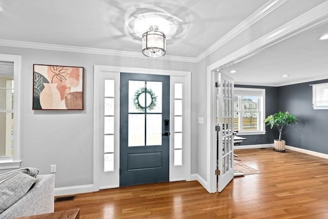 foyer with ornamental molding, visible vents, and wood finished floors