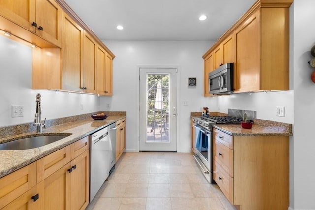 kitchen with a sink, stone counters, appliances with stainless steel finishes, and light brown cabinetry