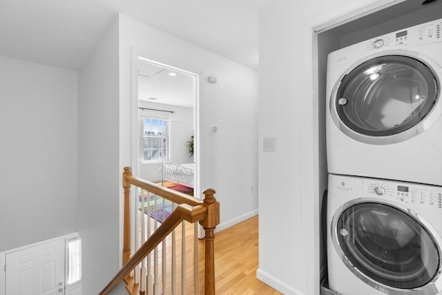 washroom with laundry area, light wood finished floors, recessed lighting, baseboards, and stacked washer / dryer
