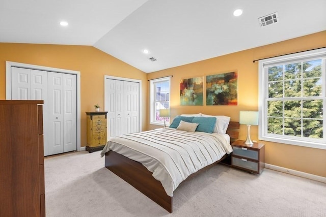bedroom with light colored carpet, two closets, lofted ceiling, and visible vents