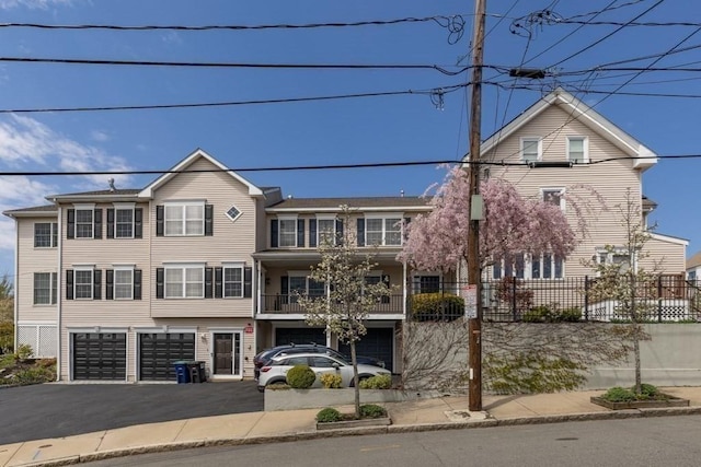view of property featuring fence, aphalt driveway, a balcony, and a garage