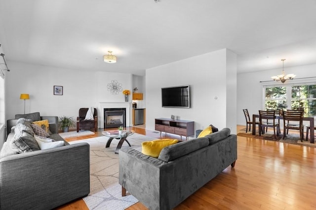 living area with an inviting chandelier, a fireplace, and light wood-style flooring