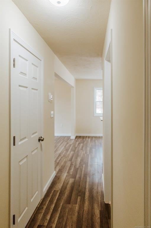 corridor featuring baseboards and dark wood-style floors