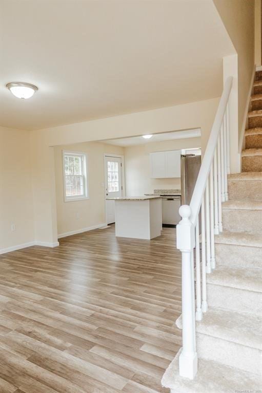 unfurnished living room with stairway, baseboards, and light wood-style flooring