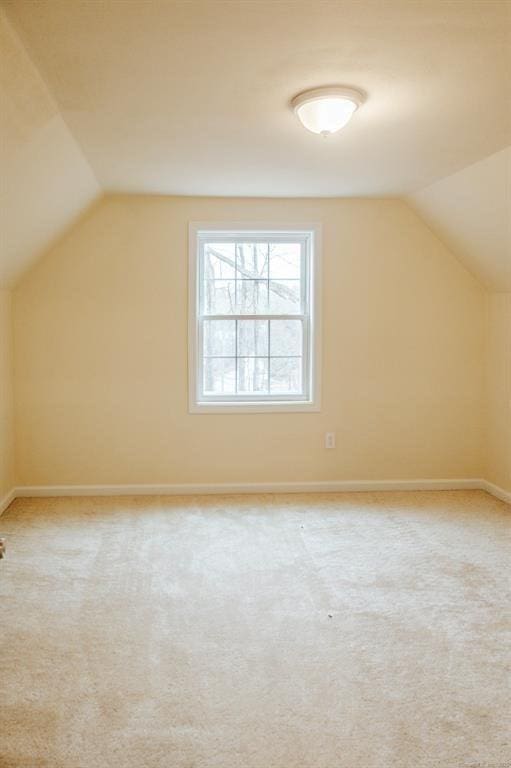 bonus room with vaulted ceiling, light colored carpet, and baseboards