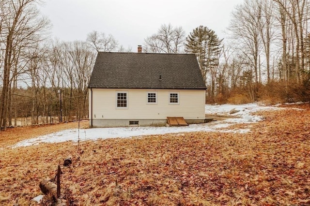 snow covered house with a chimney and roof with shingles