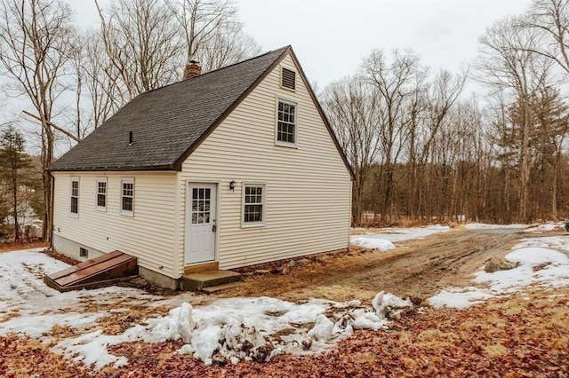 view of snow covered exterior featuring entry steps, a chimney, and roof with shingles