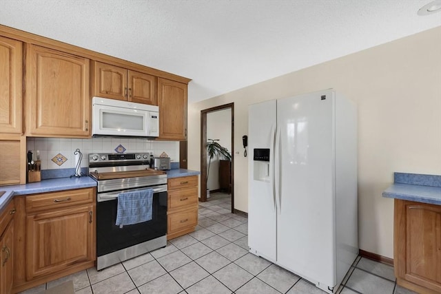 kitchen with brown cabinets, light tile patterned floors, white appliances, baseboards, and decorative backsplash