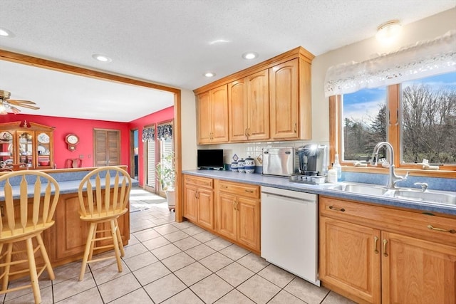 kitchen featuring white dishwasher, a sink, a breakfast bar, light tile patterned floors, and recessed lighting