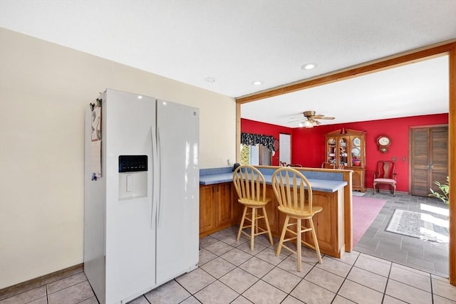 kitchen featuring a peninsula, light tile patterned flooring, recessed lighting, brown cabinets, and white fridge with ice dispenser