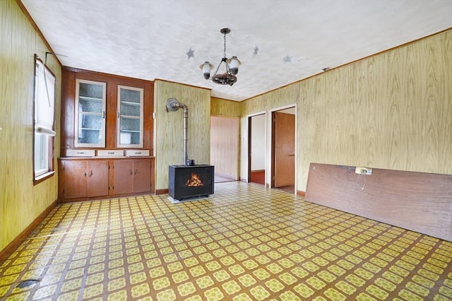 unfurnished living room with a notable chandelier, a wood stove, a textured ceiling, and wood walls