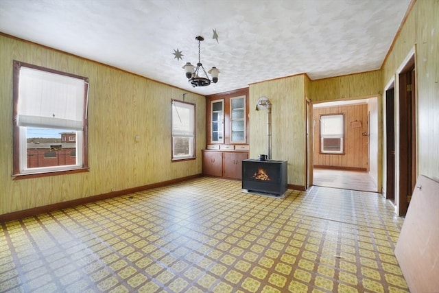 interior space featuring an inviting chandelier, ornamental molding, wooden walls, and a wood stove