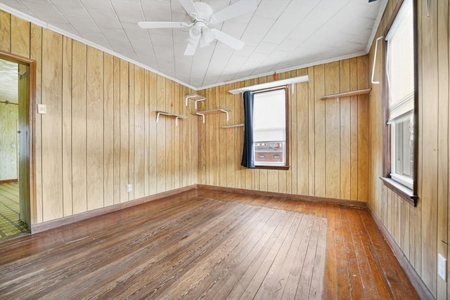 spare room with crown molding, dark wood-type flooring, ceiling fan, and wood walls