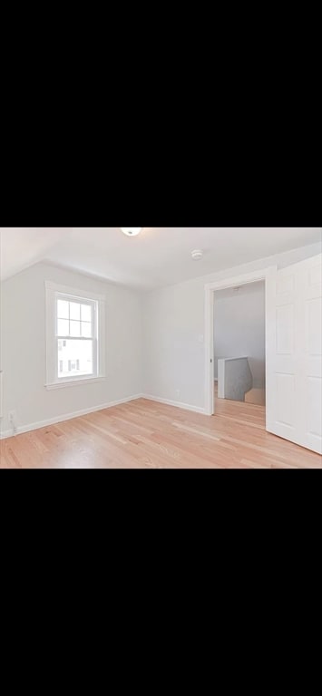 unfurnished room with light wood-type flooring and vaulted ceiling