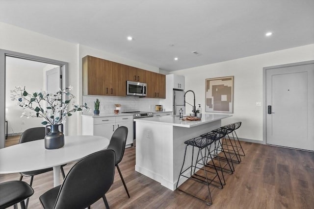 kitchen with a breakfast bar, an island with sink, a sink, stainless steel appliances, and light countertops