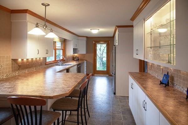 kitchen with crown molding, a sink, white cabinets, decorative backsplash, and a kitchen breakfast bar