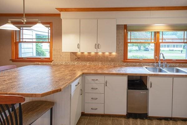 kitchen with a sink, white cabinetry, light countertops, decorative backsplash, and decorative light fixtures