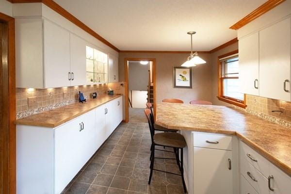 kitchen featuring crown molding, decorative backsplash, white cabinetry, a peninsula, and a breakfast bar