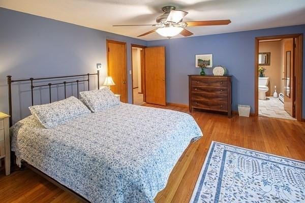 bedroom featuring wood finished floors, a ceiling fan, baseboards, and ensuite bathroom