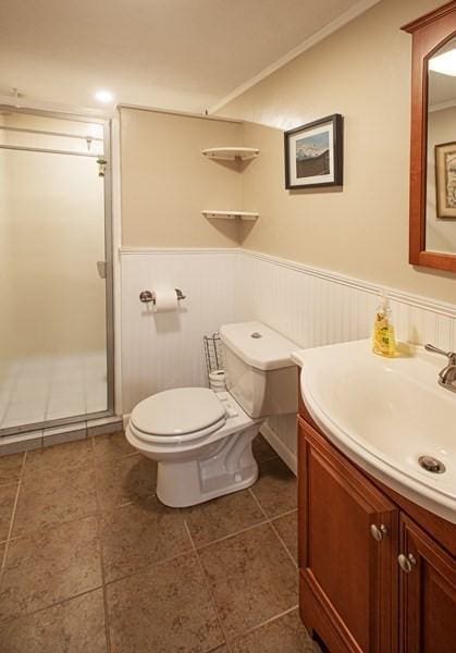 full bathroom with a stall shower, vanity, toilet, wainscoting, and tile patterned flooring