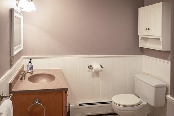 half bath with wainscoting, toilet, baseboard heating, and vanity