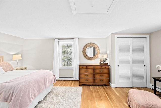 bedroom featuring a baseboard heating unit, baseboards, baseboard heating, a closet, and light wood finished floors