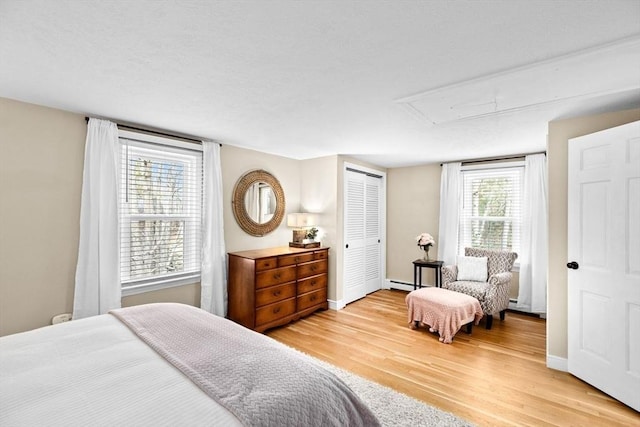 bedroom with attic access, baseboards, a baseboard radiator, light wood-style flooring, and a closet