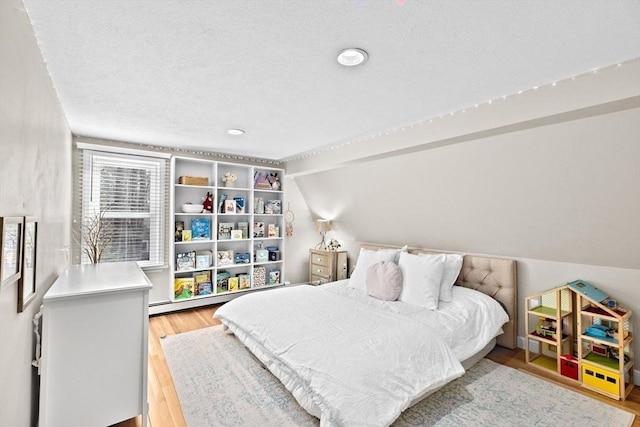 bedroom with light wood-style floors, a baseboard heating unit, vaulted ceiling, and a textured ceiling