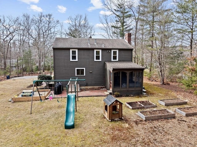 back of house featuring a sunroom, a chimney, a vegetable garden, and a playground