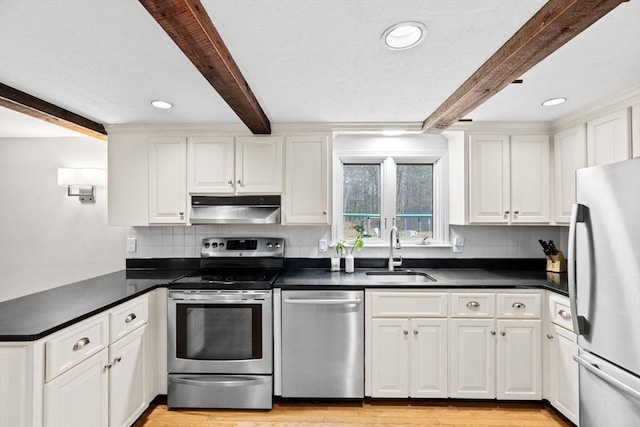 kitchen featuring under cabinet range hood, stainless steel appliances, a sink, beamed ceiling, and dark countertops