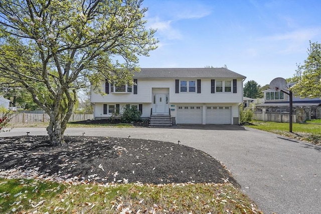 raised ranch featuring fence, an attached garage, entry steps, and driveway