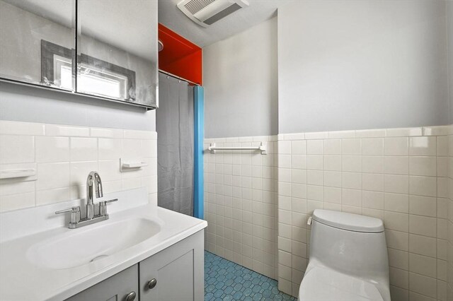 bathroom featuring visible vents, vanity, wainscoting, toilet, and tile walls