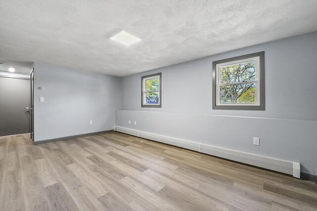 unfurnished room featuring a textured ceiling, light wood finished floors, and a baseboard radiator