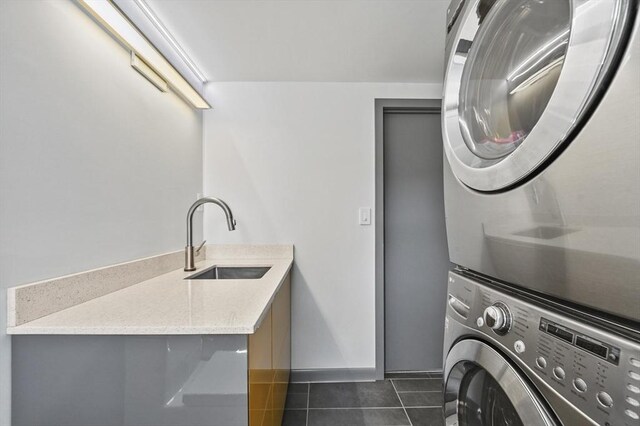 clothes washing area with laundry area, stacked washer / dryer, baseboards, dark tile patterned floors, and a sink