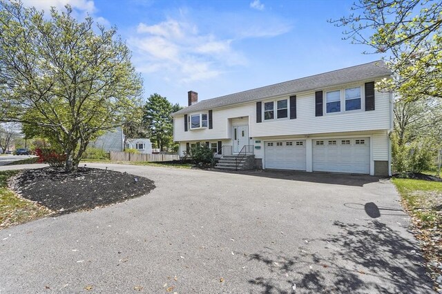 raised ranch featuring a garage, fence, a chimney, and aphalt driveway