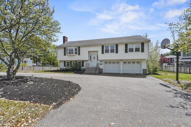raised ranch featuring fence, curved driveway, a chimney, and a garage