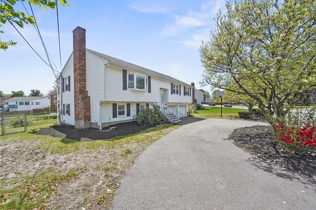 bi-level home with fence, a chimney, driveway, and a garage